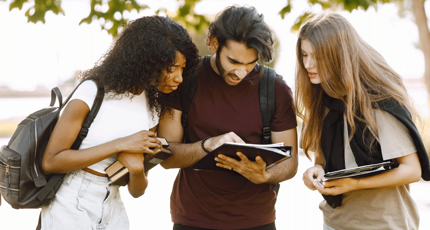 International transfer students looking at a notebook the middle student is holding