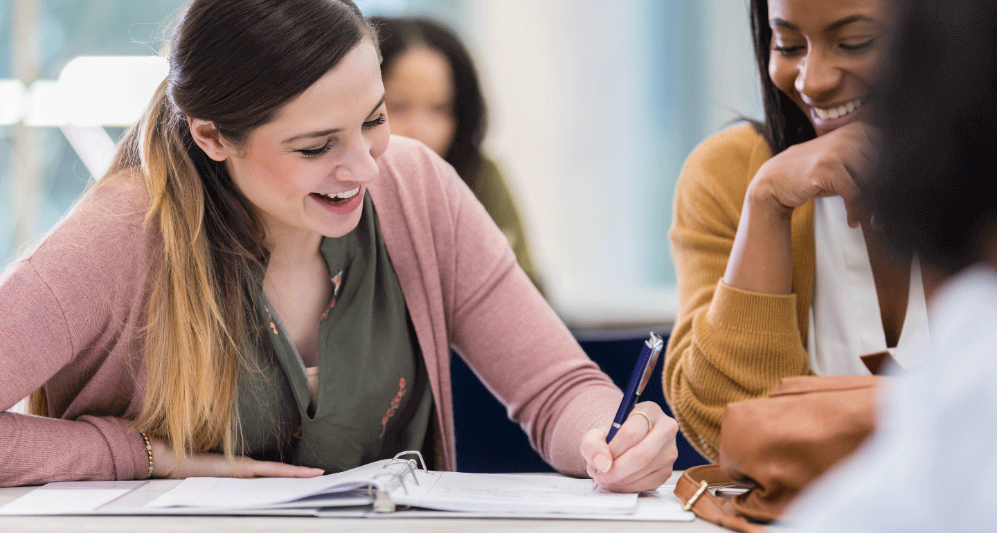 Writing program. Two female students at desk, one writing in notebook
