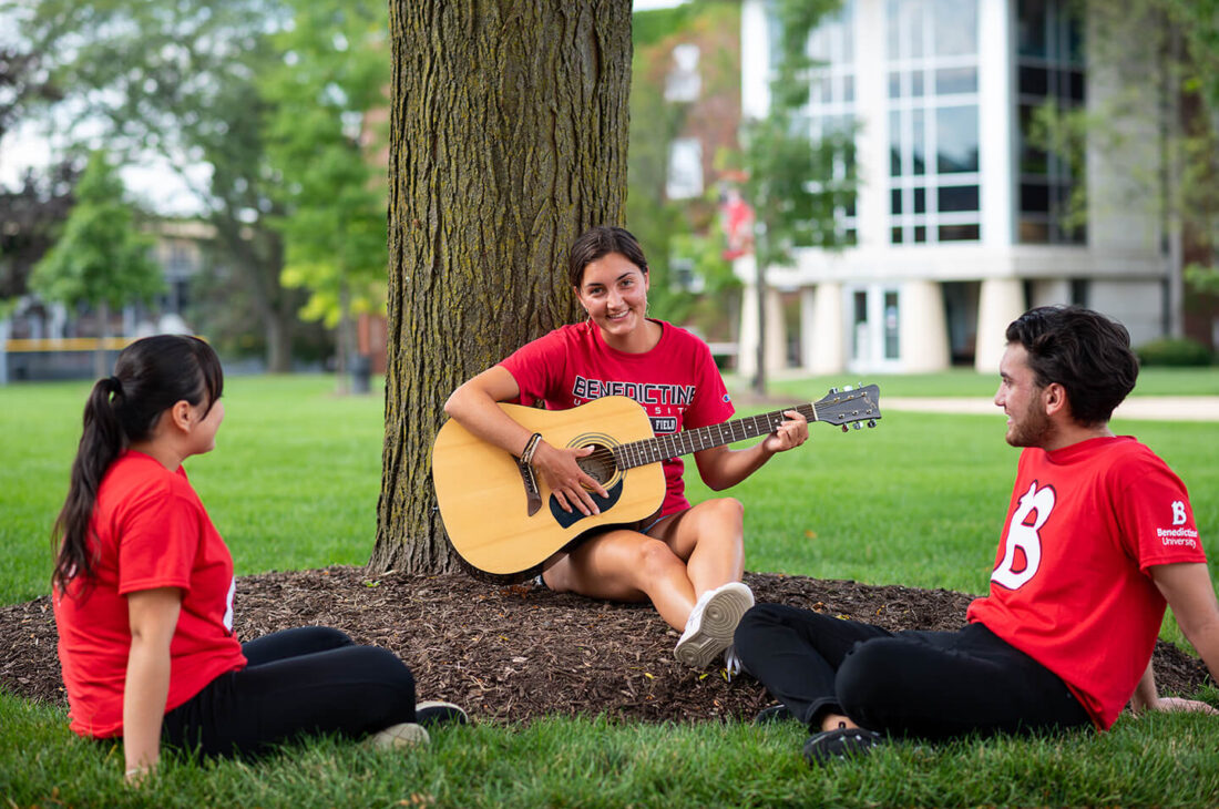 Student playing guitar on quad